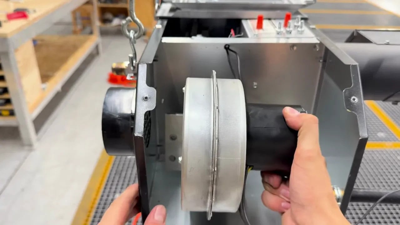 Hands positioning a fan blower inside the open heater compartment