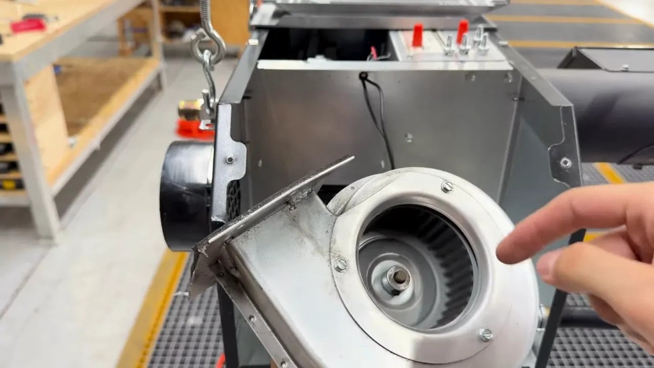 Removed blower with its circular wheel exposed and a finger pointing toward the center